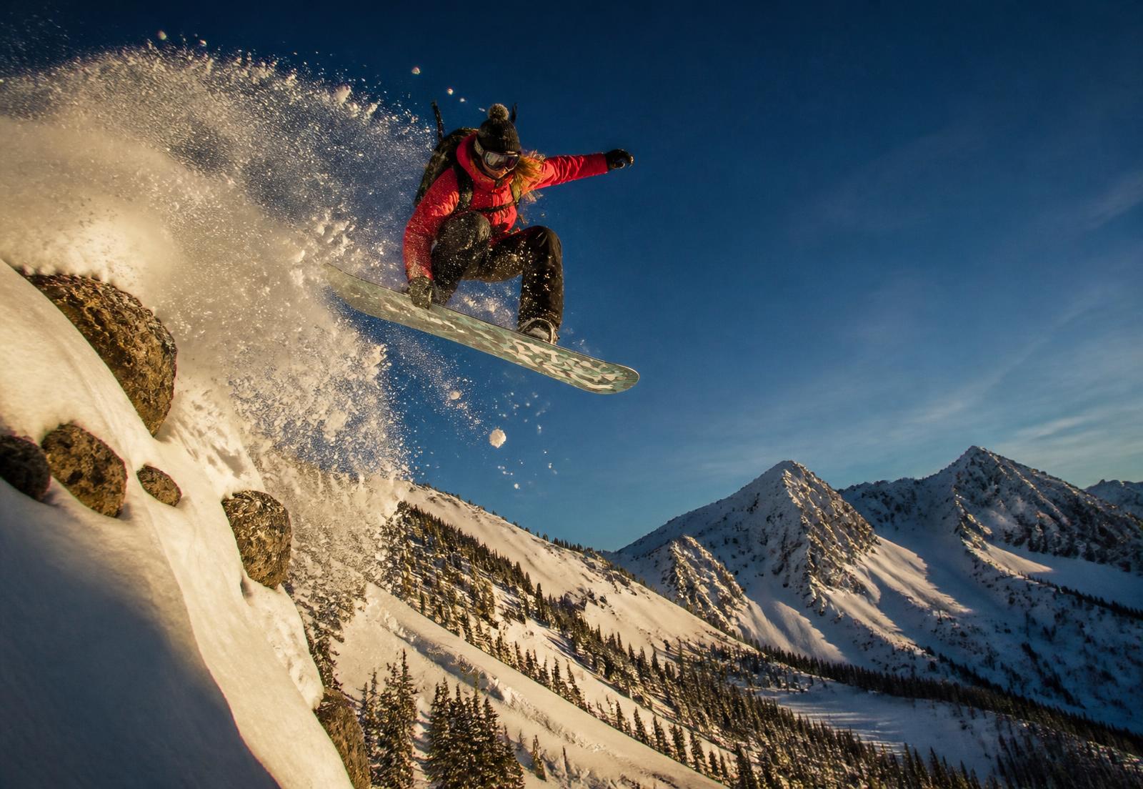 Dani launching a backcountry cliff drop on her snowboard above Park City